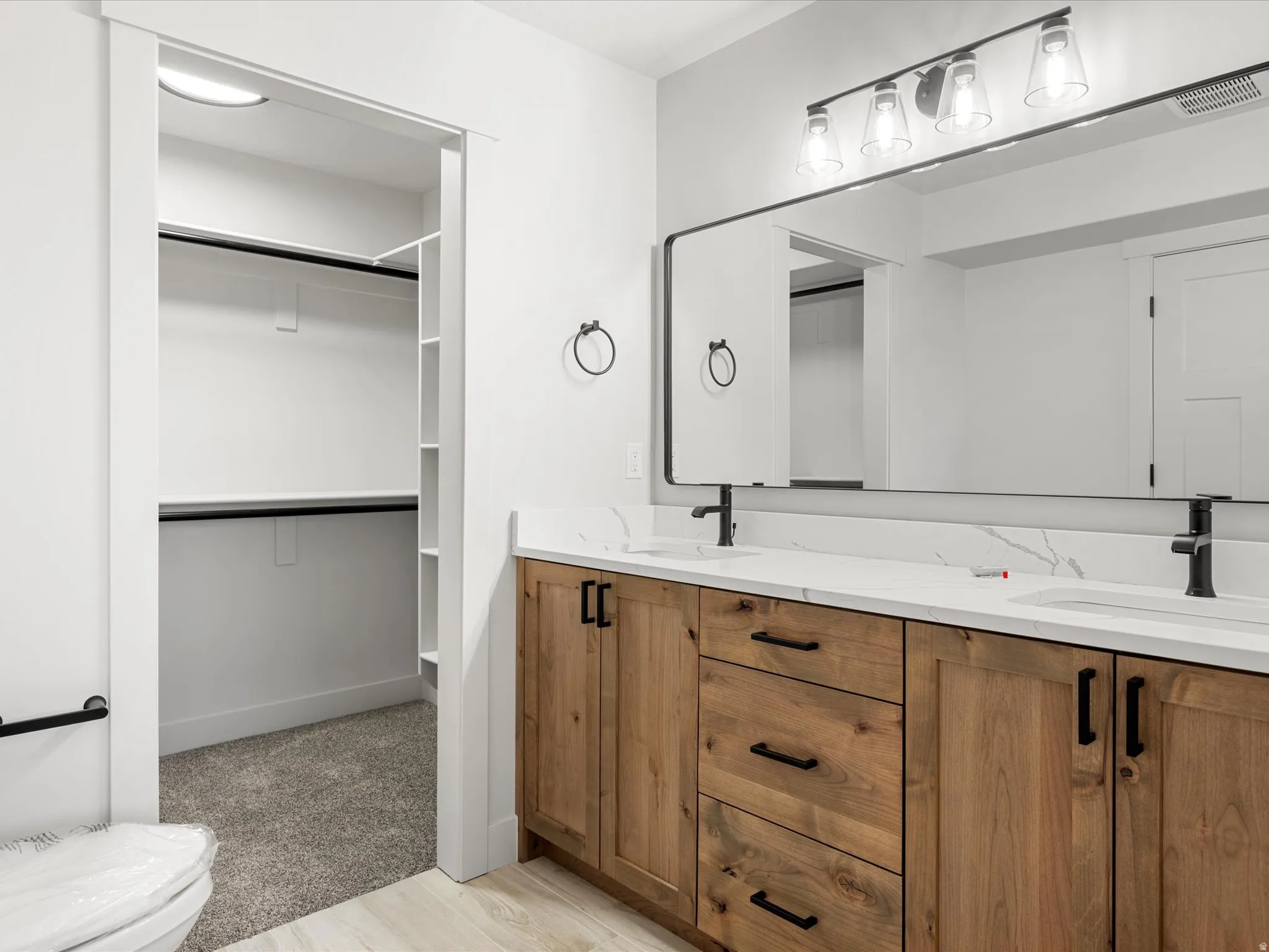Double vanity with wood-finish cabinetry, white quartz countertops, and matte black fixtures