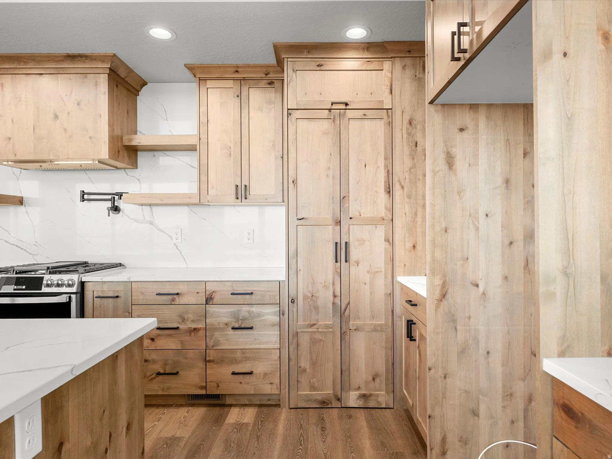 Kitchen featuring natural wood cabinetry, white countertops, a contrasting white and gray veined backsplash, and recessed lighting