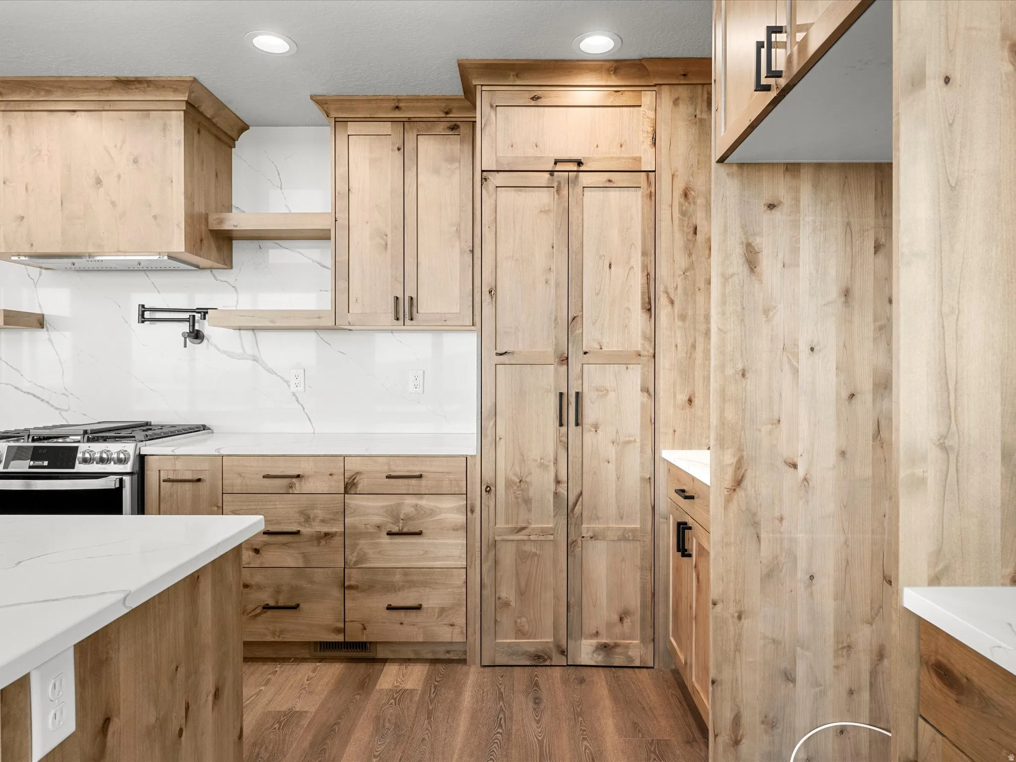 Modern kitchen featuring wood cabinetry, white countertops, a gas range with an overhead vent hood, a pot filler, and recessed lighting