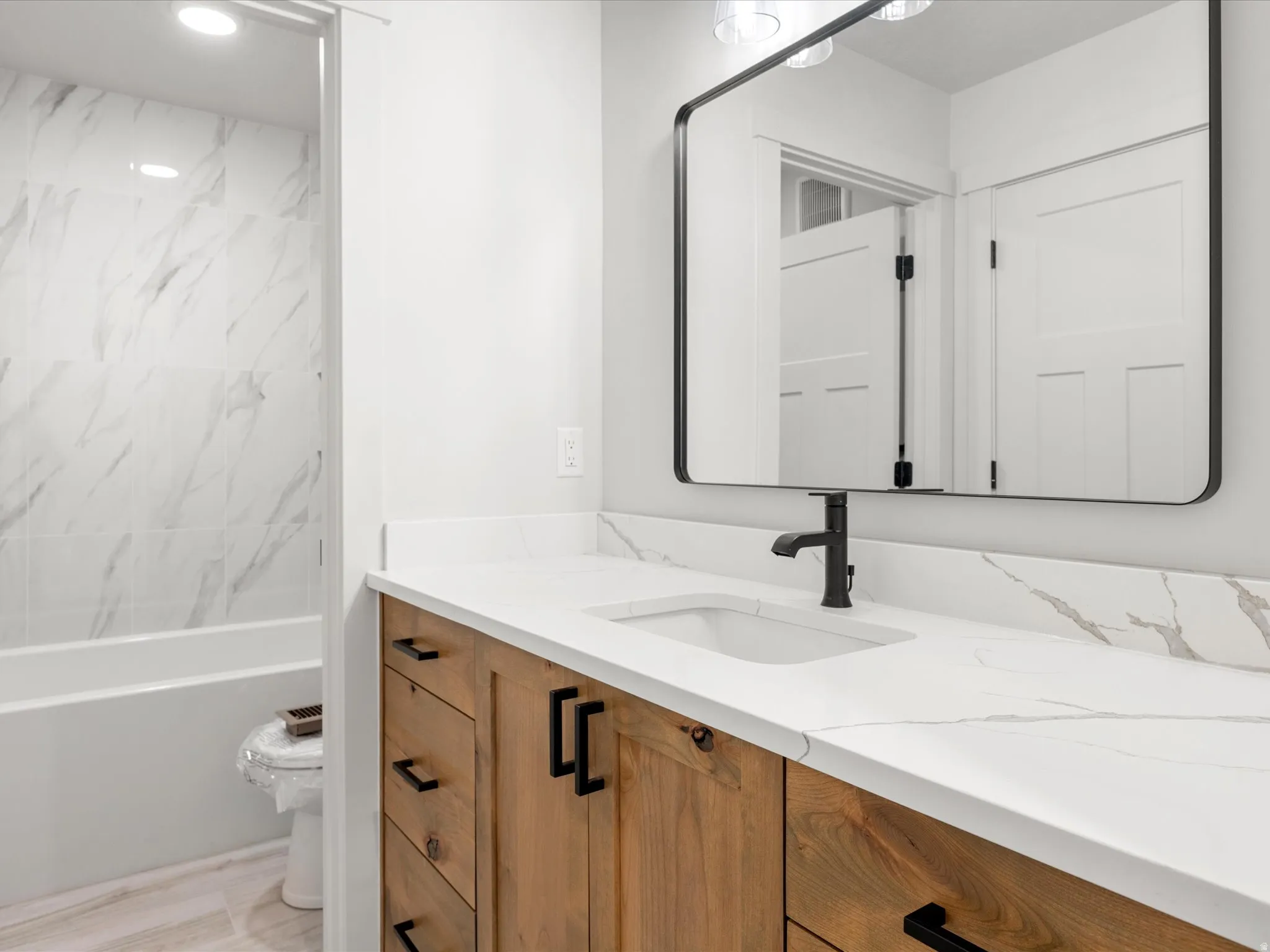 Bathroom featuring a wood-finish vanity with black hardware, a white countertop with integrated sink, and a rectangular black-framed mirror