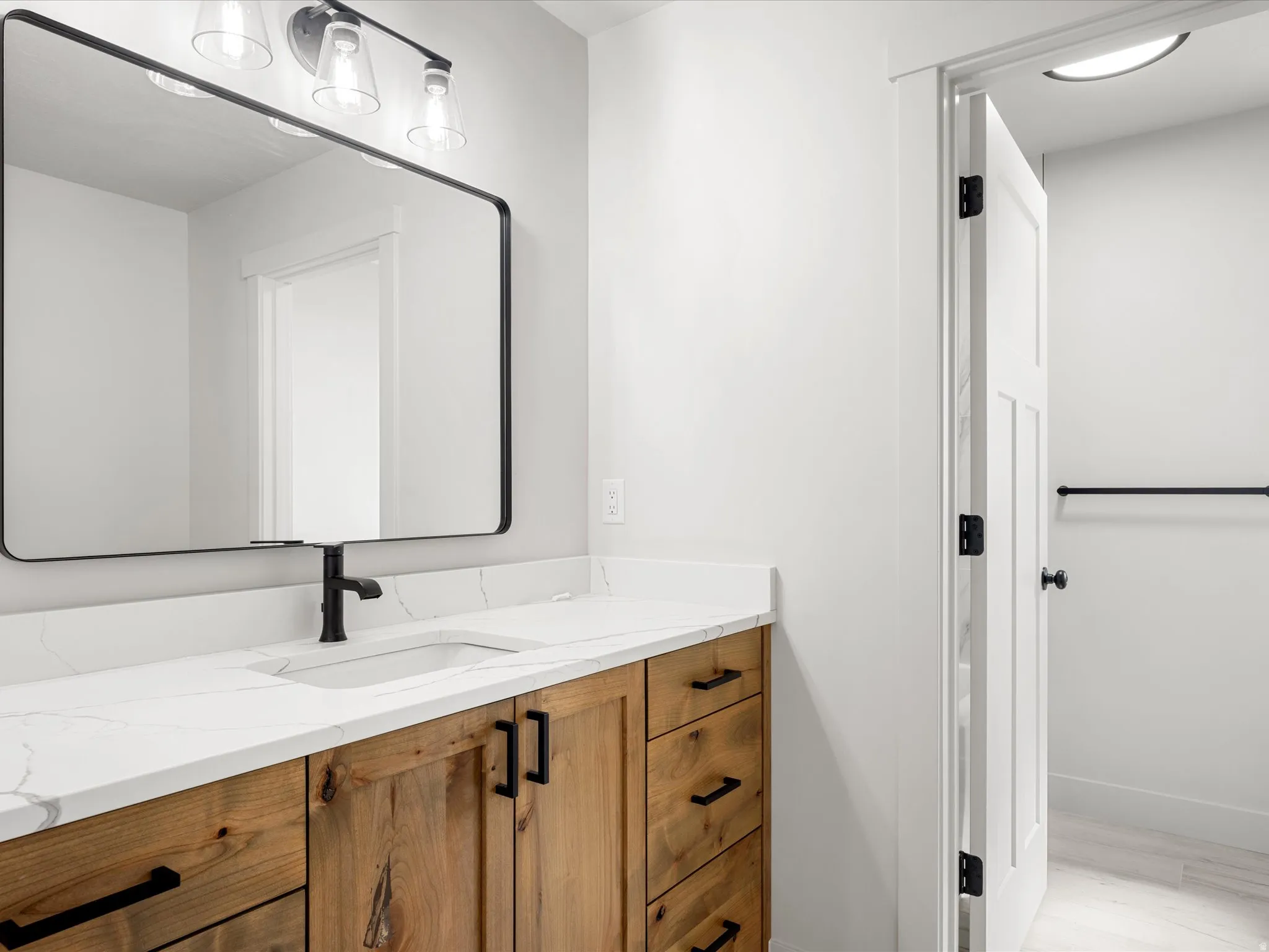 Bathroom vanity featuring a wood-finish cabinet, white countertop with integrated sink, and matte black hardware