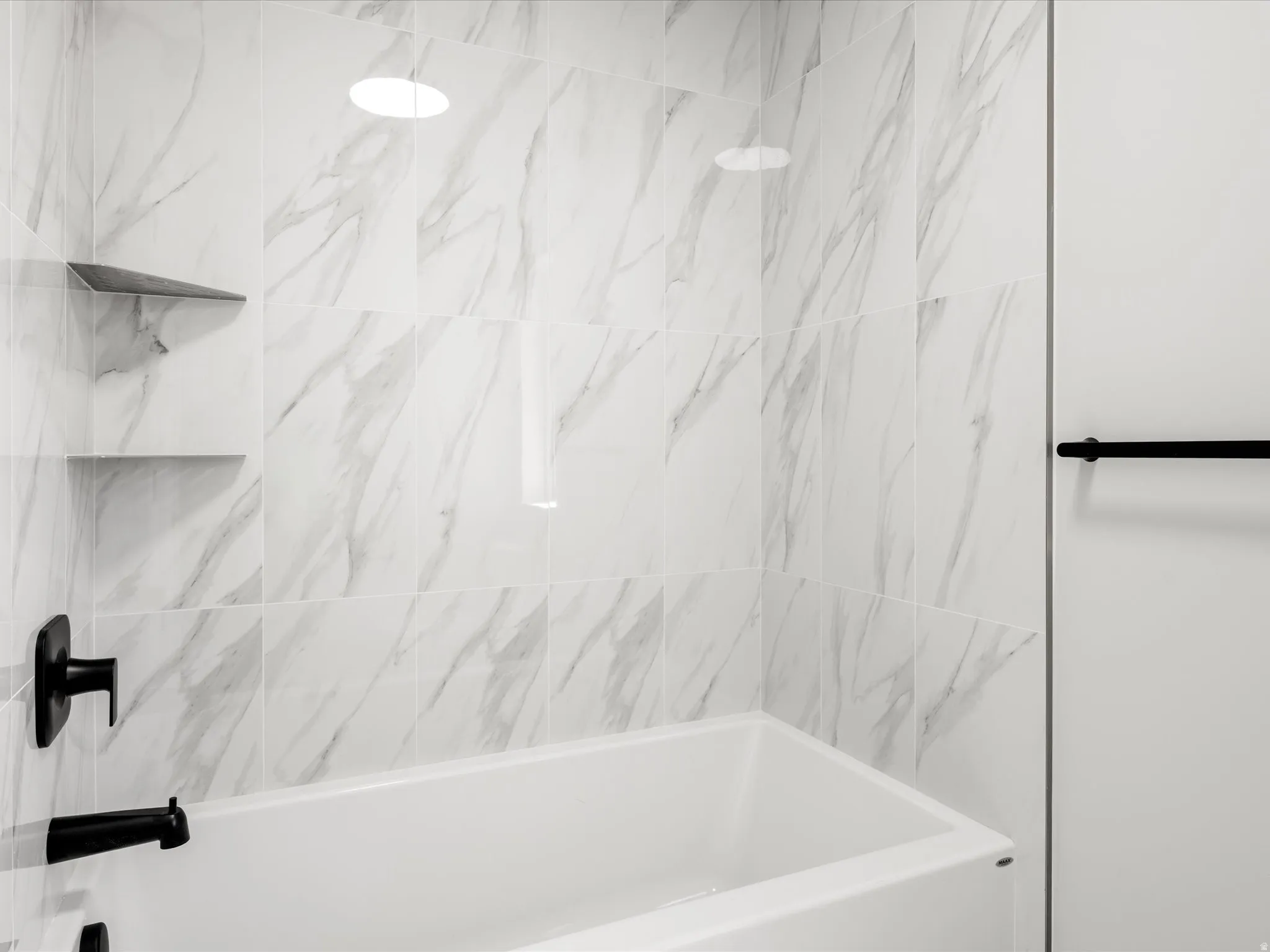 White bathtub with matte black fixtures, surrounded by large format marble-look tile