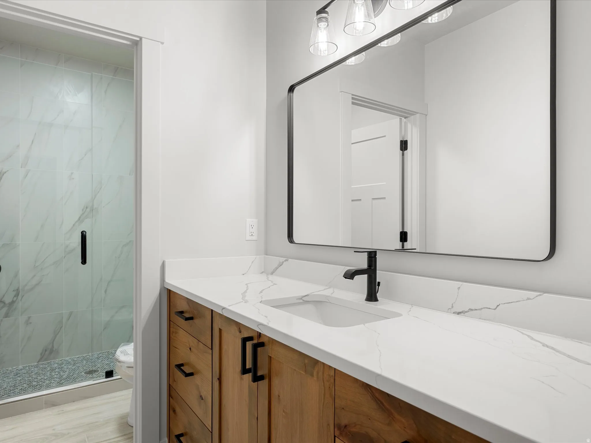 Contemporary bathroom featuring a wood-finish vanity with matte black hardware, a rectangular undermount sink, and a white countertop with subtle veining