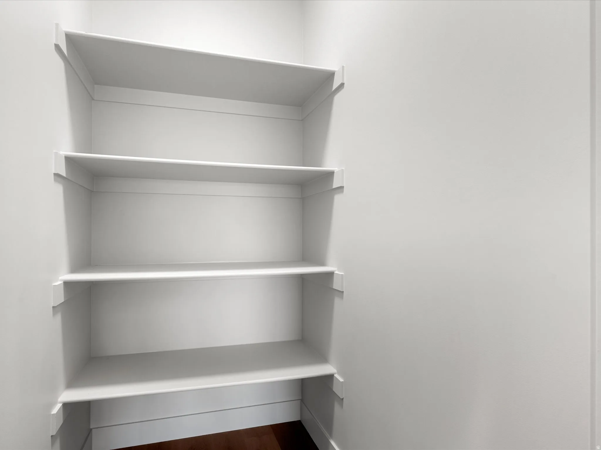 Built-in white shelving system with five levels of storage, integrated baseboard trim, and dark wood-finish flooring