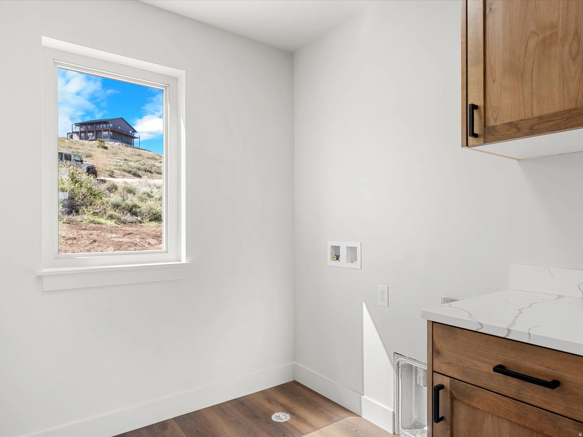Laundry area featuring wood-finish flooring, a single window, white walls, and built-in wood cabinetry with a white countertop