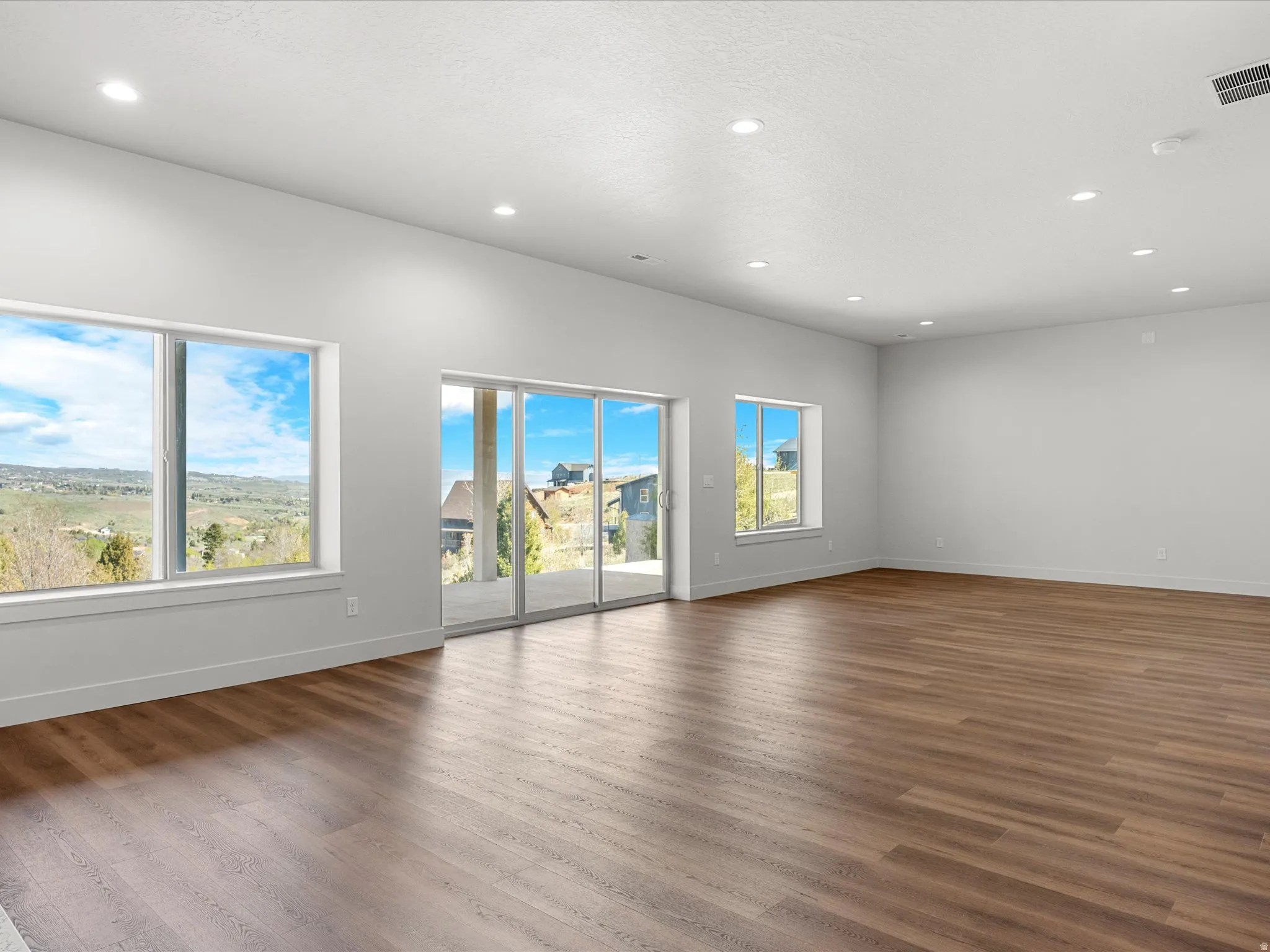 Spacious interior with wood-finish flooring, recessed lighting, white walls, and broad windows
