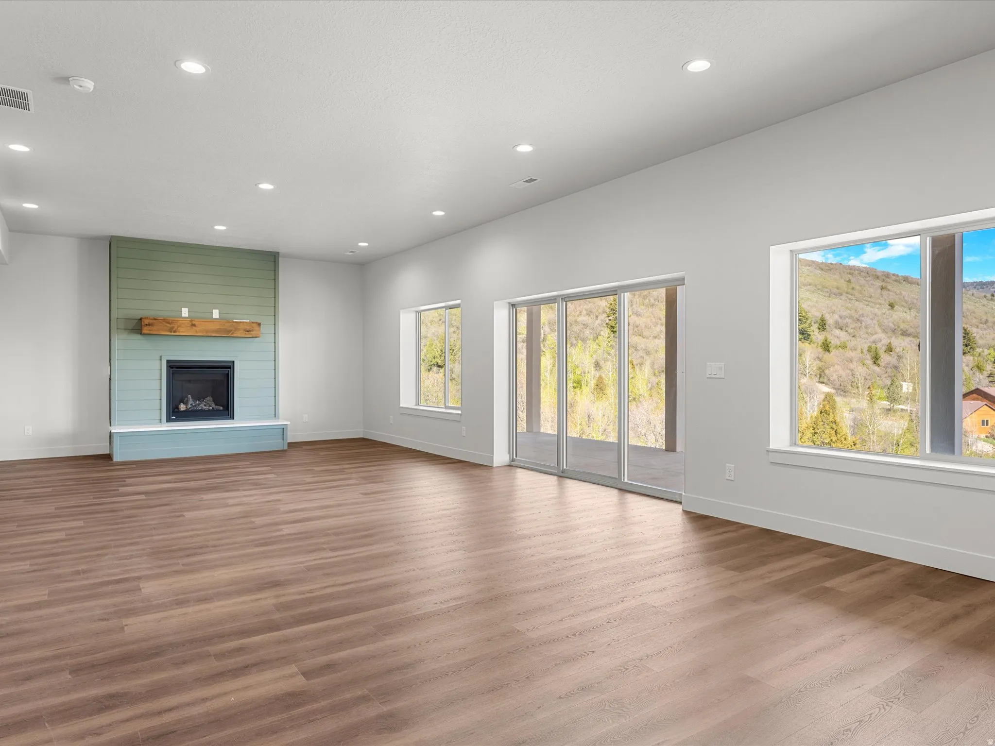 Spacious interior featuring wood-finish flooring, a contemporary fireplace with a wood mantle and shiplap accent wall, recessed lighting, and large windows with sliding glass doors