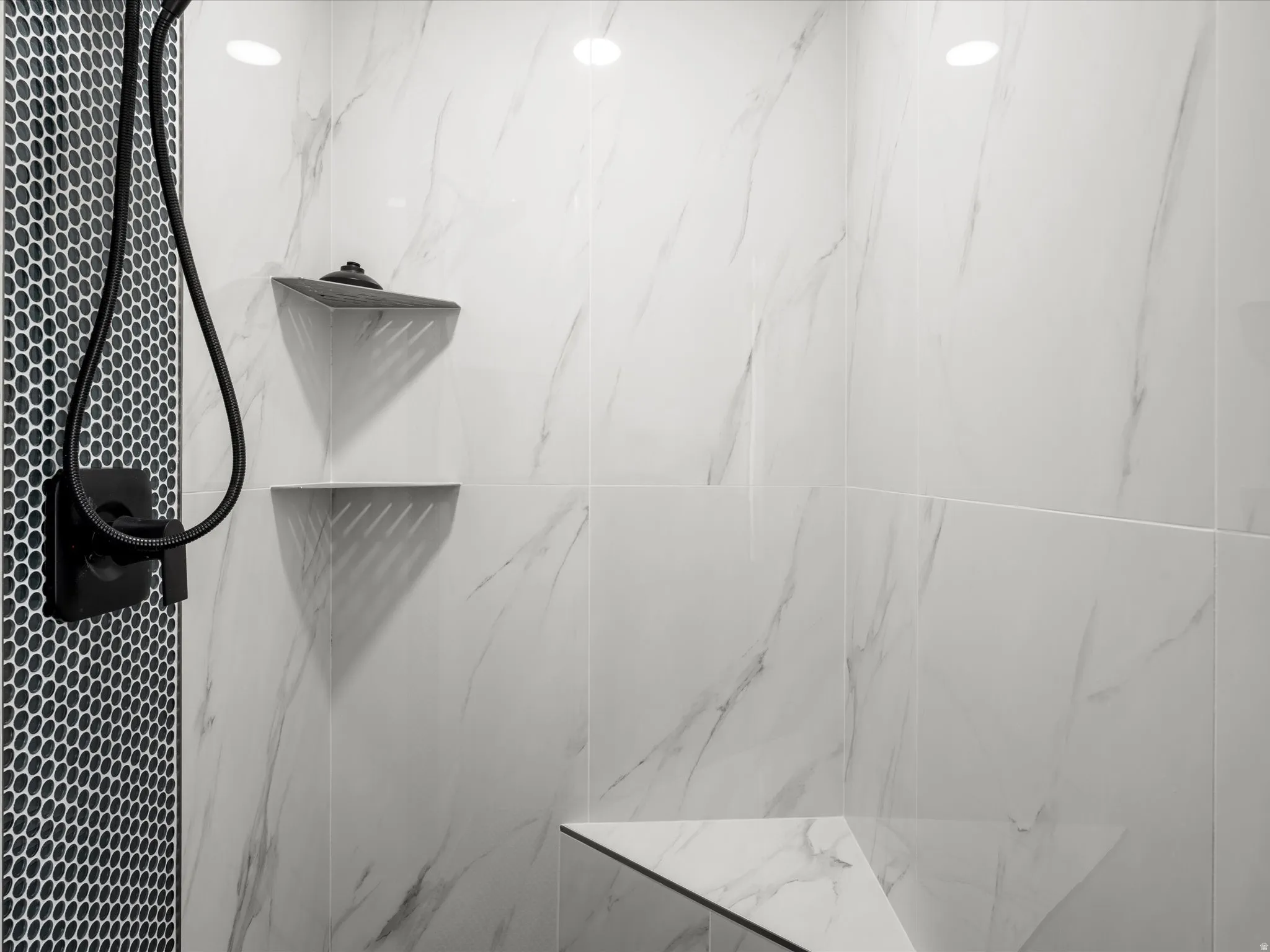Primary Shower with white vein-patterned wall tiling, a black hexagonal tile accent wall, built-in corner shelves, a built-in shower bench, and a matte black shower fixture