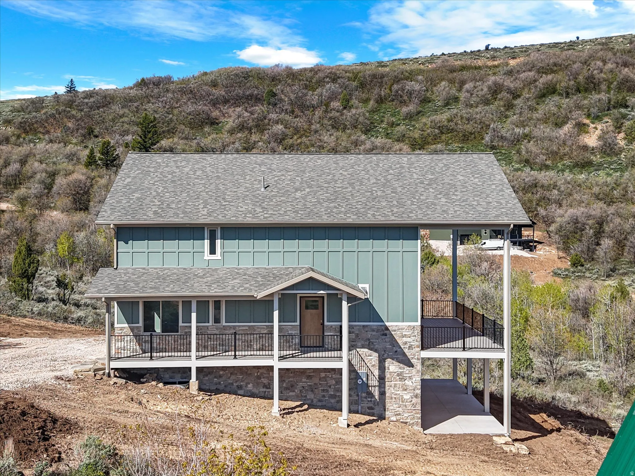 Two-story home featuring a gray shingle roof, light blue vertical siding, and a stone facade foundation