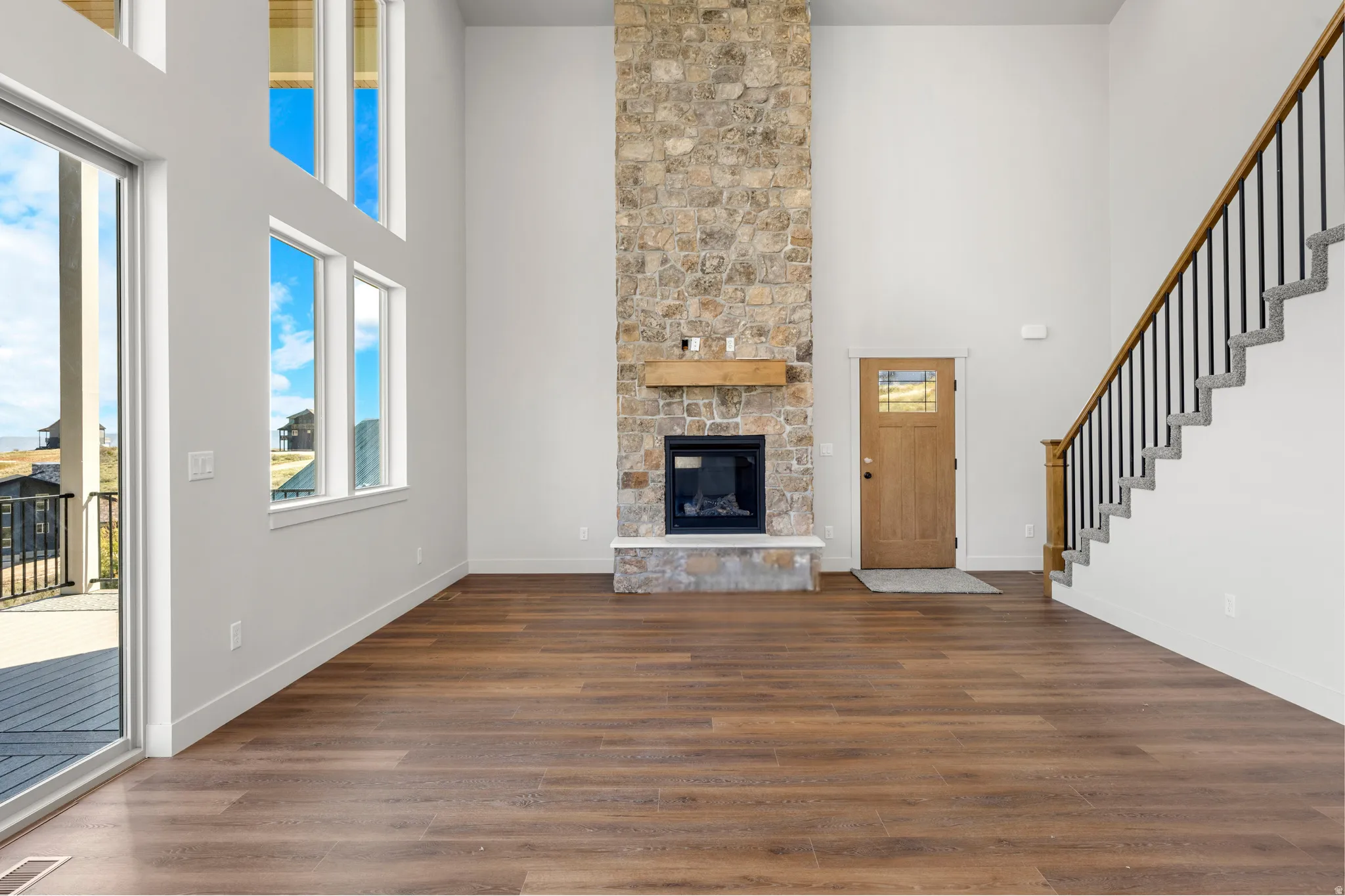 Spacious living area featuring a floor-to-ceiling stone fireplace, wood-finish flooring, and a multi-level window arrangement