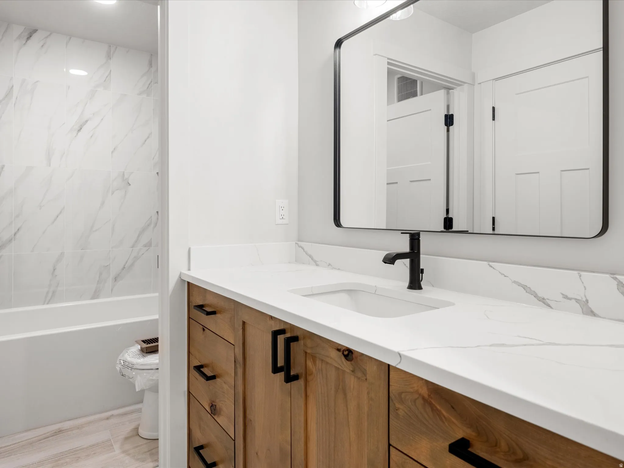 Modern bathroom featuring a wood-finish vanity with black hardware, a white countertop with gray veining, and an undermount sink with a matte black faucet