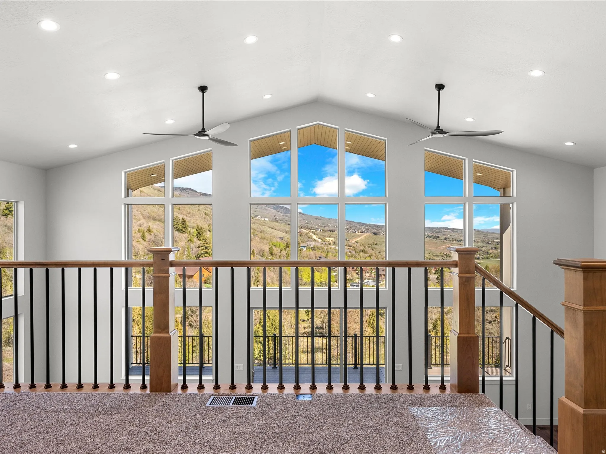 Loft with large picture windows, recessed lighting, and wood-finish railing with black balusters