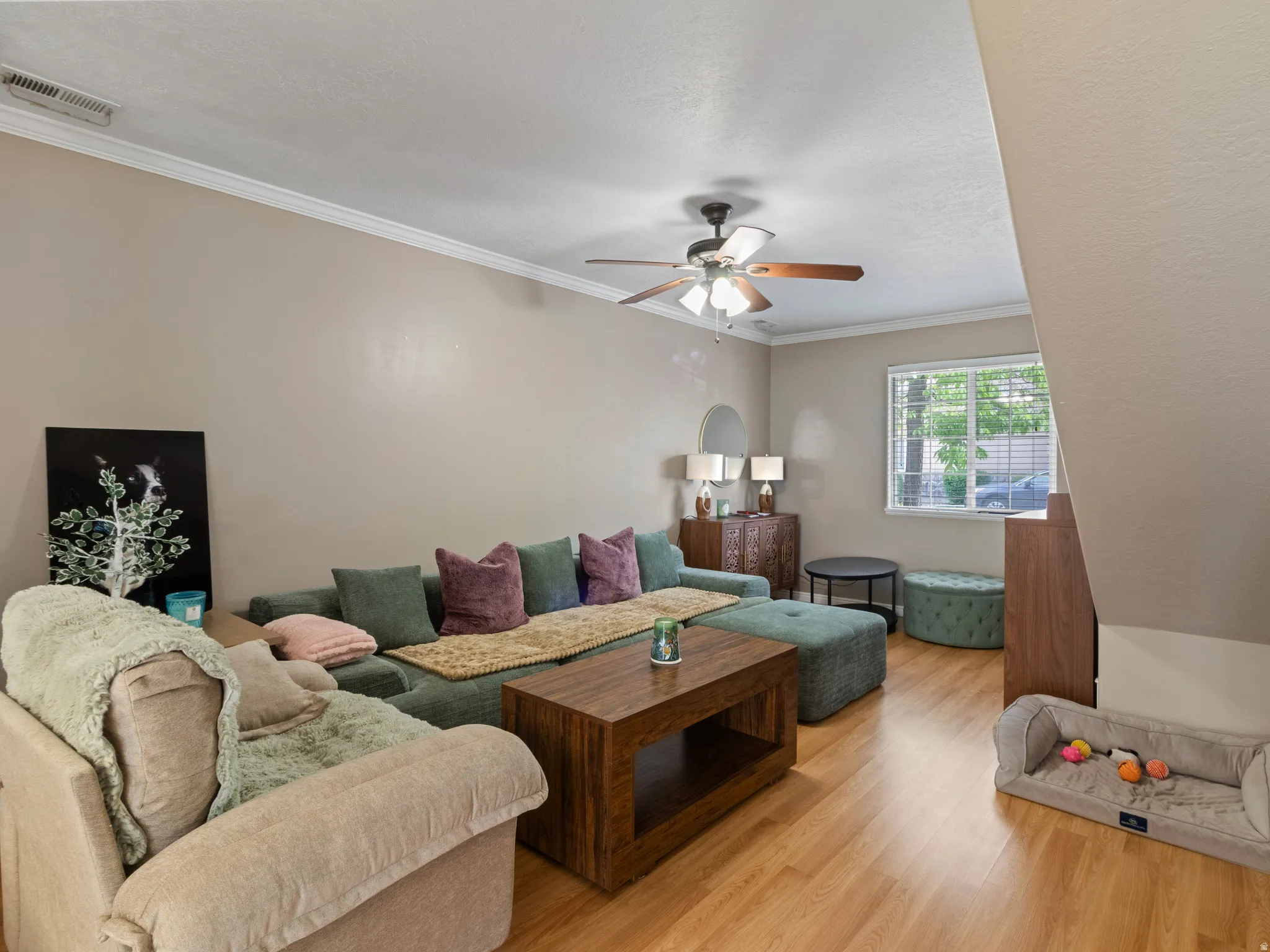 Living area featuring wood-finish flooring, a ceiling fan with light fixture, and crown molding