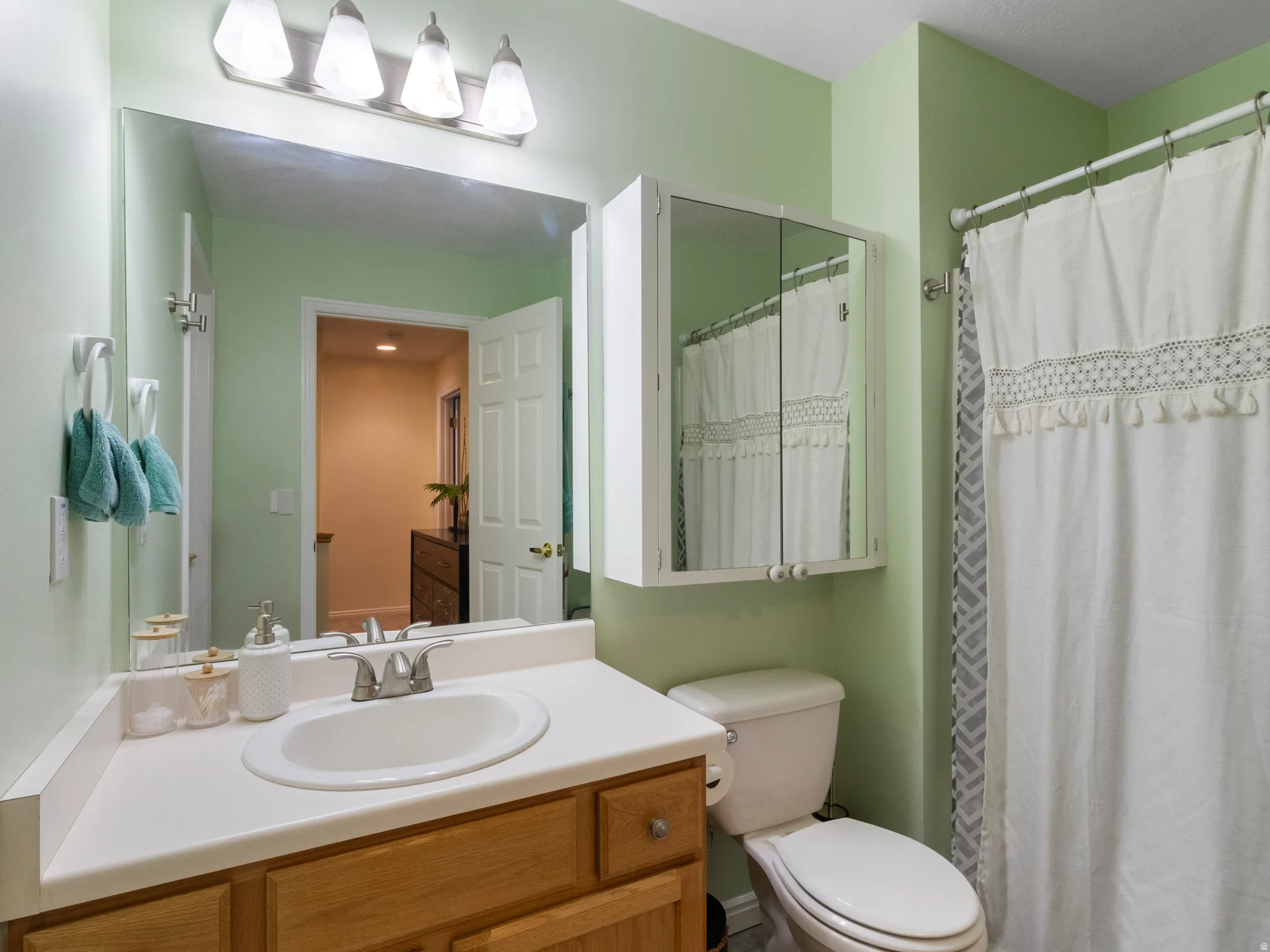 Bathroom featuring a wood-finish vanity with a white countertop and integrated sink, a large wall-mounted mirror, and a four-light vanity fixture