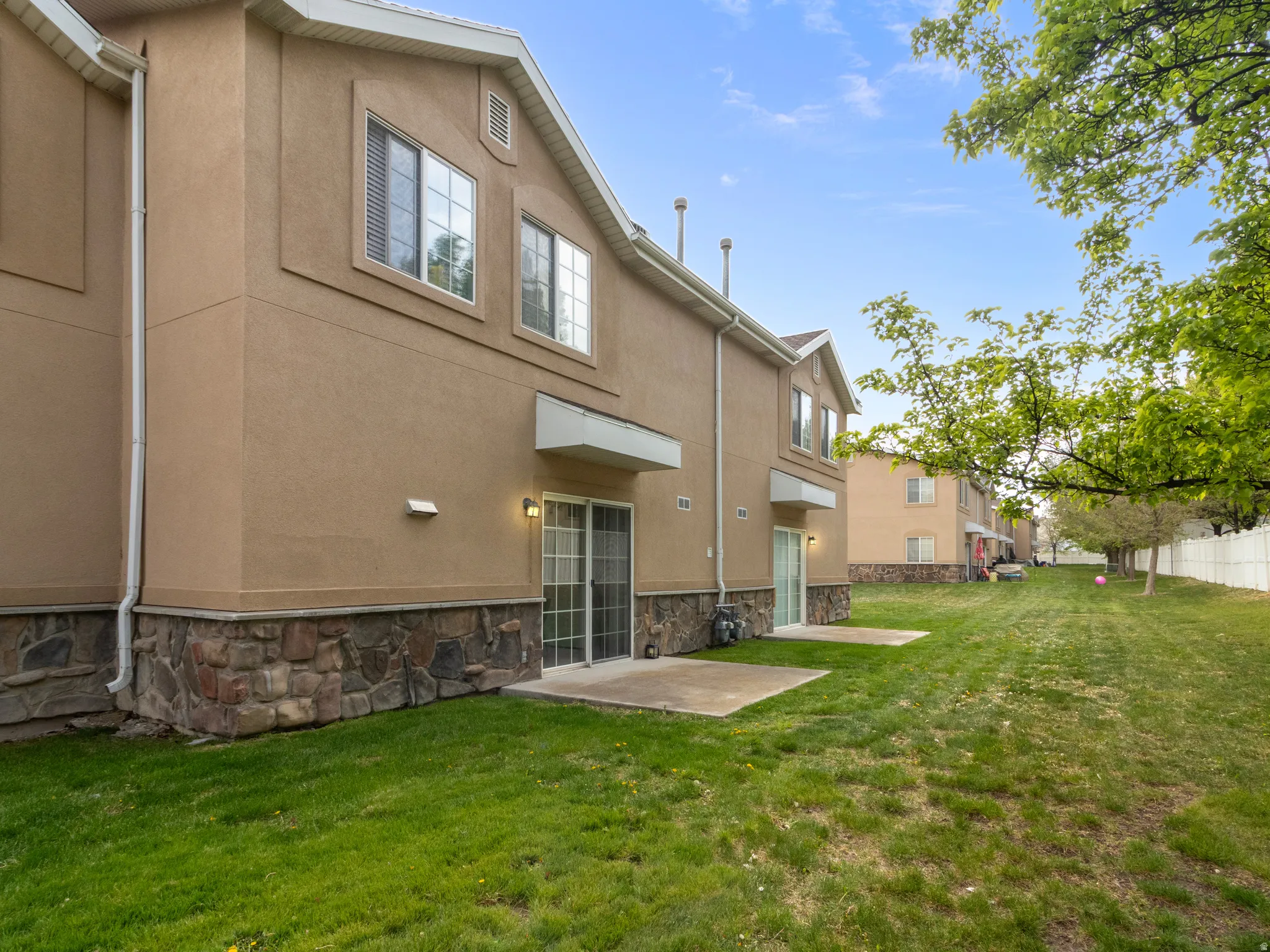 Rear exterior featuring two concrete patios, sliding glass doors, stucco siding, and a stacked stone foundation