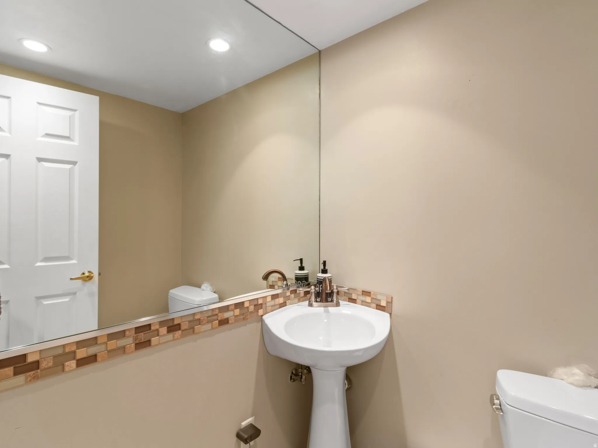 Pedestal sink with mosaic tile backsplash, large wall-mounted mirror, and recessed lighting