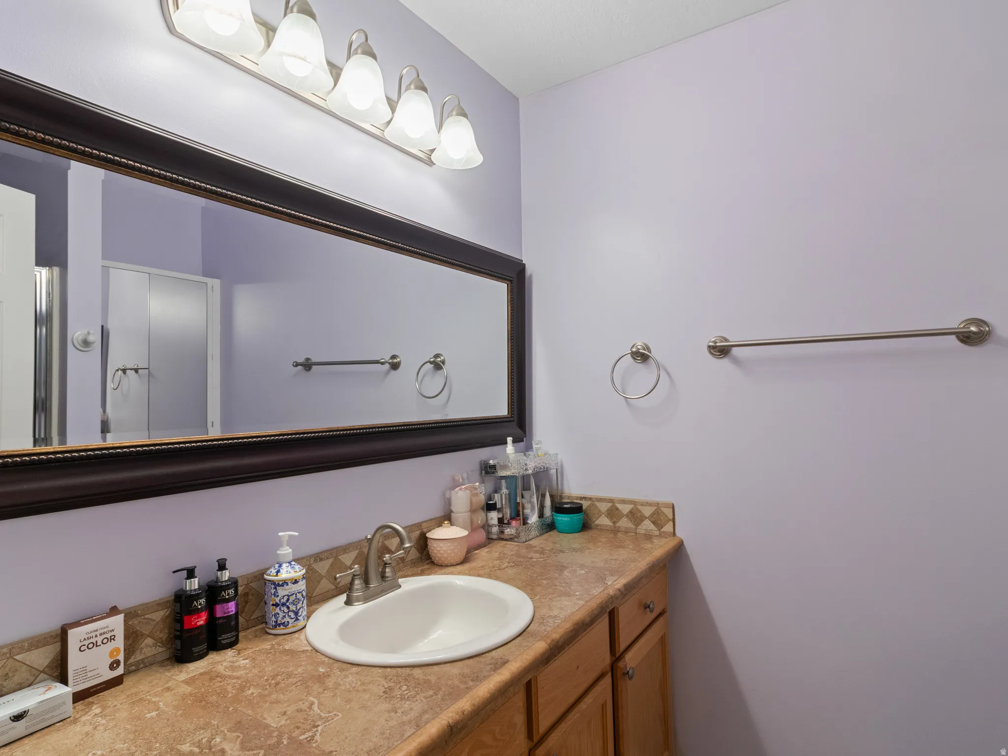 Vanity featuring an integrated sink, brushed nickel faucet, and a large framed mirror with overhead lighting