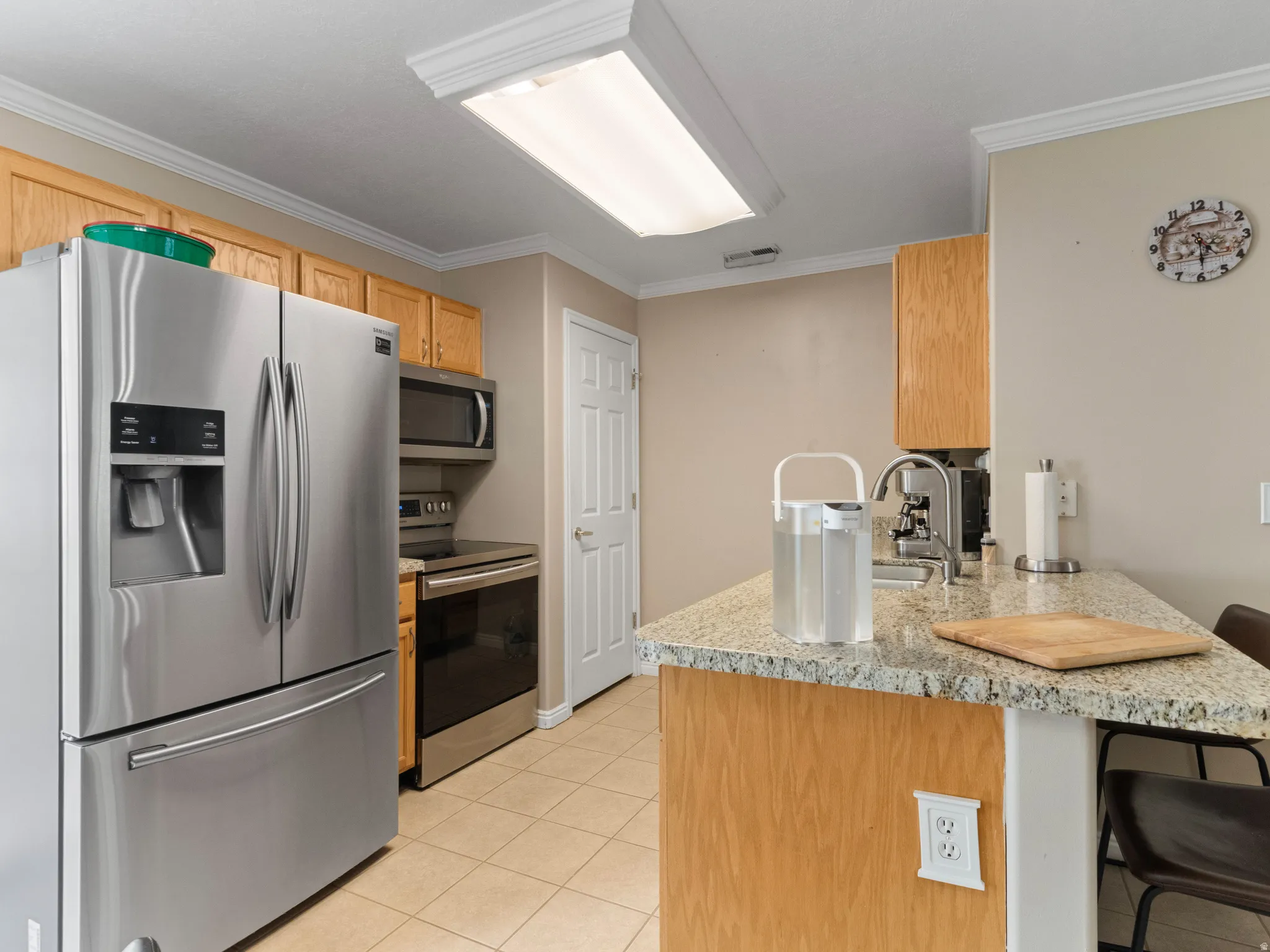 Kitchen featuring granite-style countertops, wood-finish cabinetry, stainless steel appliances, tile flooring, and crown molding
