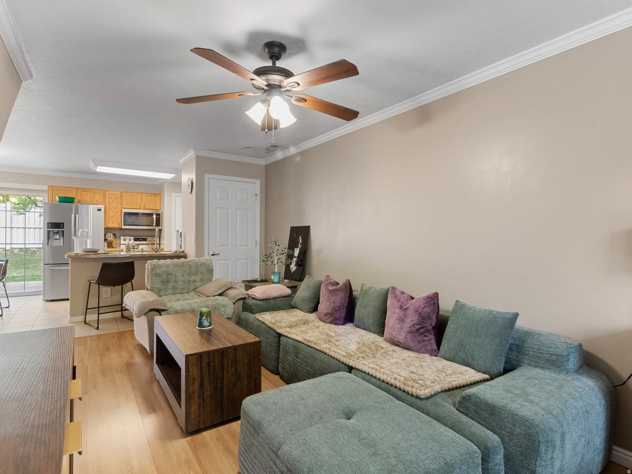 Open concept living space featuring wood-finish flooring, crown molding, and a ceiling fan with integrated lighting