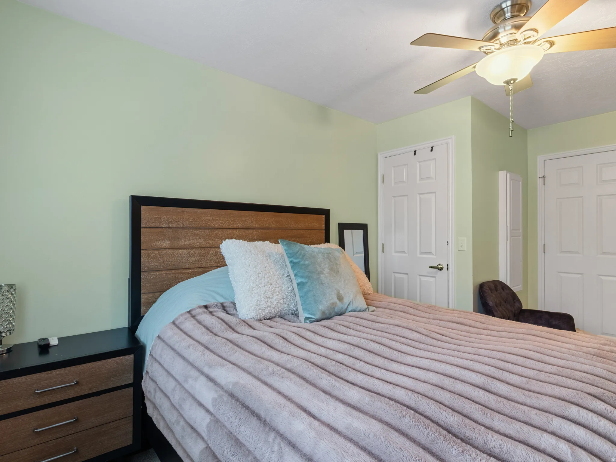 Bedroom featuring light green walls, a ceiling fan with integrated lighting, and two paneled interior doors