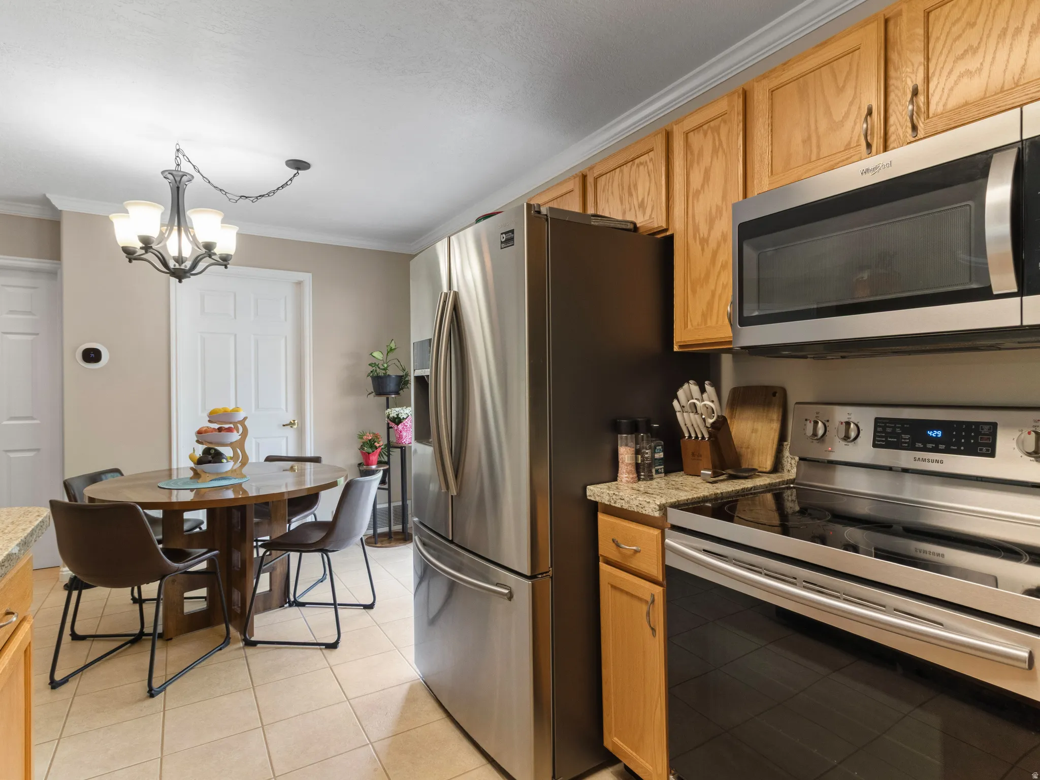Kitchen featuring stainless steel appliances, wood cabinetry, granite-style countertops, and a tile floor