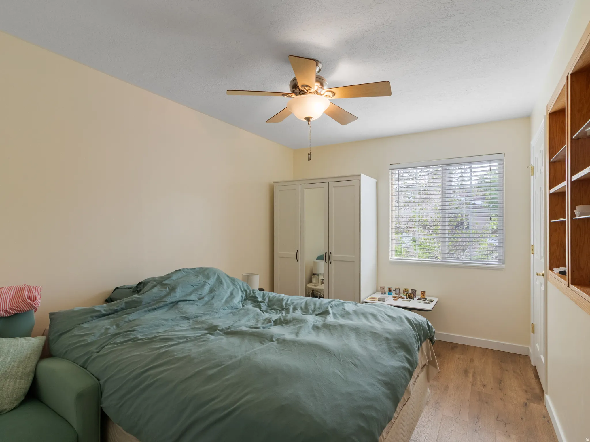 Room with wood-finish flooring, a ceiling fan with integrated lighting, and a window featuring blinds