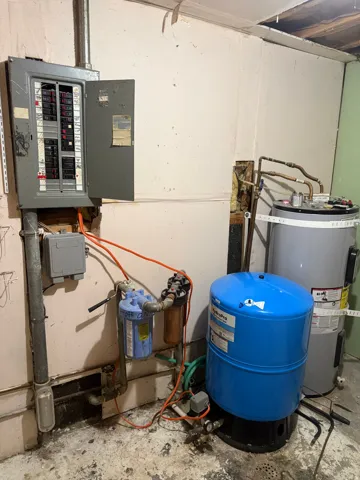 Electrical panel with exposed wiring, water heater, water filtration system, and blue pressure tank