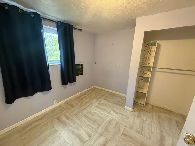 Bedroom featuring light-toned tile flooring, a window, and a built-in closet with shelving and a hanging rod