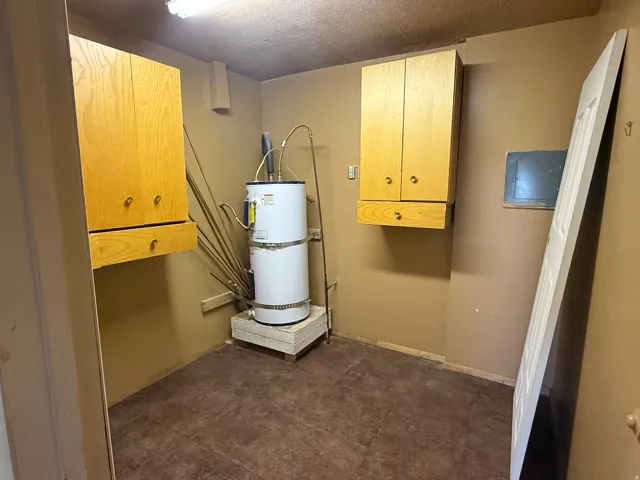 Utility room with a water heater, two wall-mounted wood-finish cabinets, and brown flooring