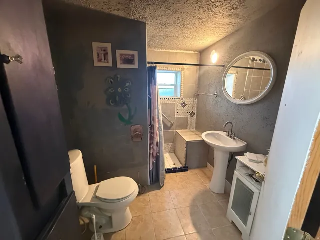 Bathroom featuring a pedestal sink, round wall mirror, and a shower with built-in bench seating