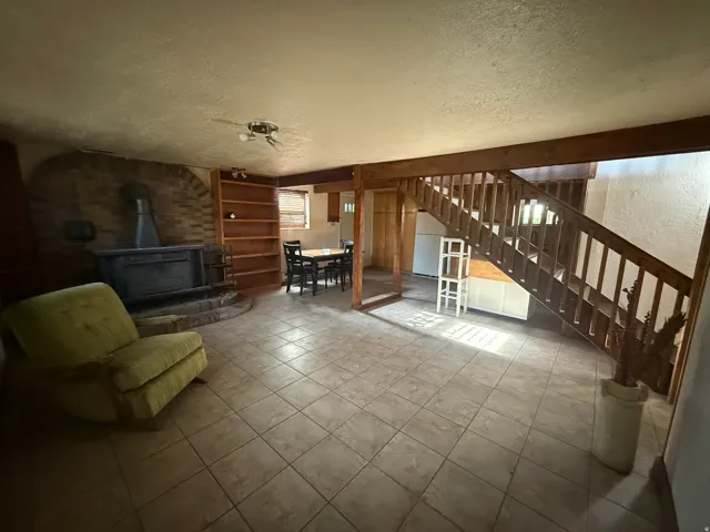 Open-concept living space with tile flooring throughout, featuring a brick-surround wood-burning stove, built-in shelving, and a wooden staircase