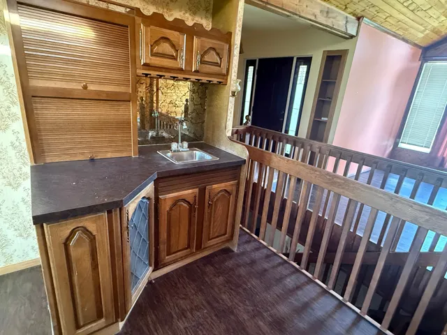 Built-in wet bar with a stainless steel sink, wood cabinetry, and a mirrored backsplash