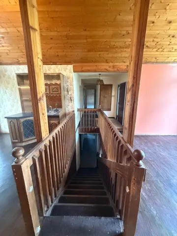 Exposed wood-finish ceiling, detailed wooden banister, wood-finish flooring, built-in cabinetry with diamond-patterned glass, and an overhead light fixture
