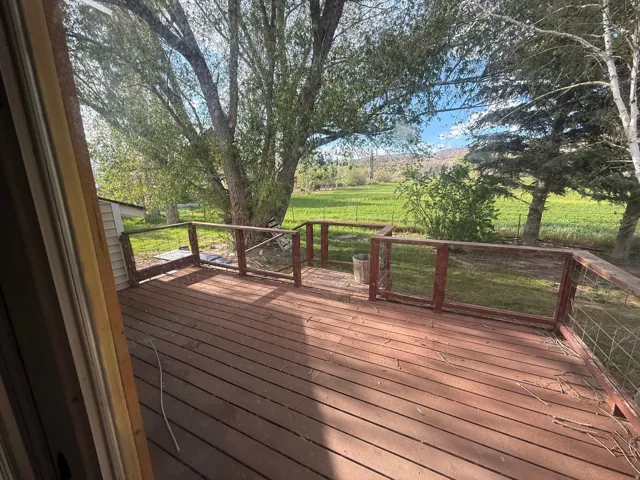 Spacious outdoor wood deck with wire fencing, surrounded by mature trees, and overlooking expansive green terrain