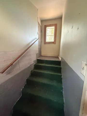 Staircase featuring green carpet treads, a wood handrail, and a framed window at the landing