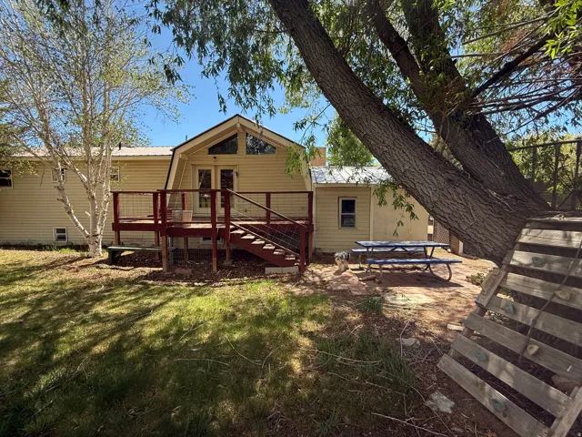 Rear exterior featuring a spacious wood deck with metal railing, vaulted ceiling with transom windows, and dual glass French doors