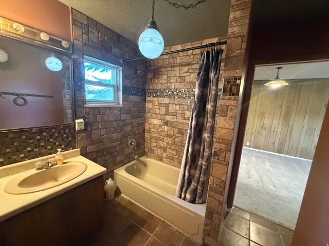 Bathroom featuring a single vanity with built-in sink, tiled flooring, and a bathtub with a tiled surround
