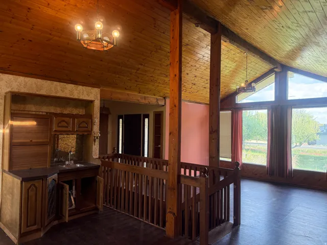 Vaulted wood-paneled ceiling with exposed beams, full-height windows, a built-in wet bar, wood-finish flooring, and a wooden banister