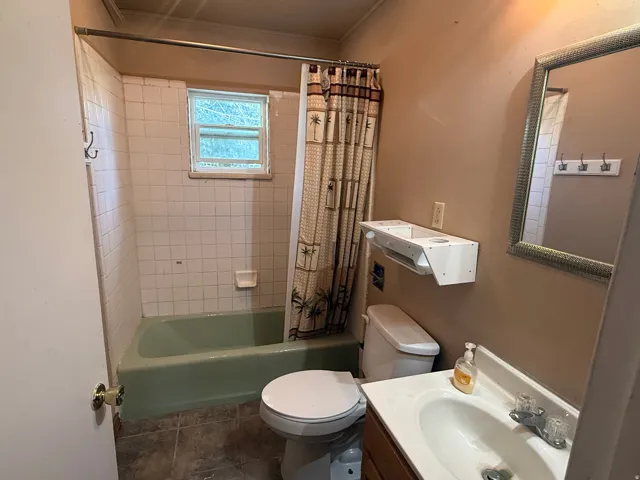Bathroom featuring a bathtub with tiled surround, a single window, a toilet, a vanity with an integrated sink, and an ornamental mirror