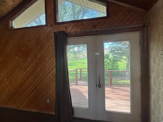 Double glass-paneled doors opening to an exterior deck, complemented by diagonal wood-paneled walls and a matching wood-paneled ceiling