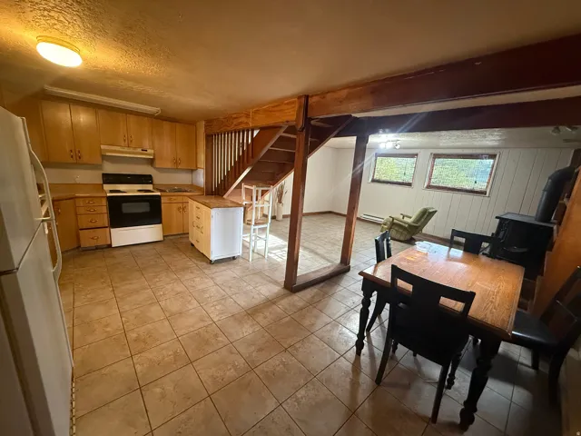 Kitchen and living area featuring tile flooring, wooden cabinetry, an electric range, and a wood-burning stove