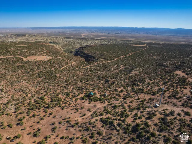 Expansive desert landscape featuring a single-story structure with a green roof, a communications tower, and unpaved access paths