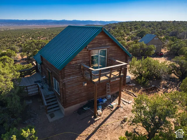 Log cabin exterior featuring a green metal roof, a second-story wood deck, and an expansive wood-plank deck with stairs