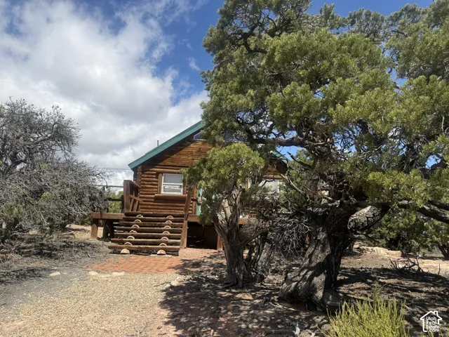 Log cabin exterior with a green metal roof, elevated wood deck with railing, and a stone paver patio area