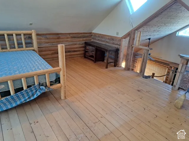 Vaulted ceiling with wood-finish paneling, skylights, wood-finish flooring, and log-style wall detailing