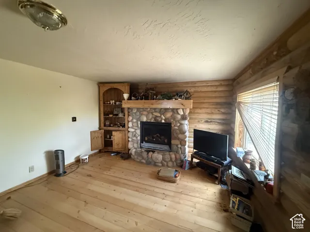 Living area featuring a stone-clad fireplace with a wooden mantel, natural wood-finish flooring, and log-style interior walls