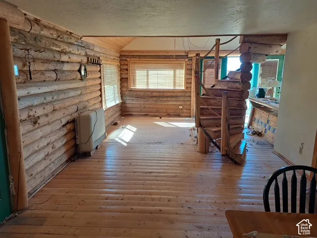 Log wall construction, wood-finish flooring, natural wood spiral staircase, and multiple windows with blinds