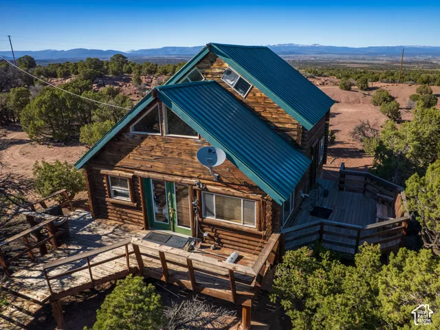 Log cabin exterior featuring a vibrant green metal roof, multiple windows, and a prominent front deck