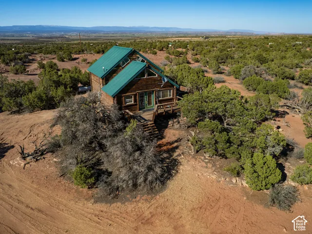 Log cabin exterior with a green metal roof, multiple windows, and a wooden deck