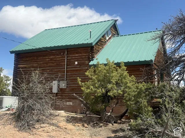 Log cabin exterior featuring a green metal roof, natural wood siding, and visible electrical conduit